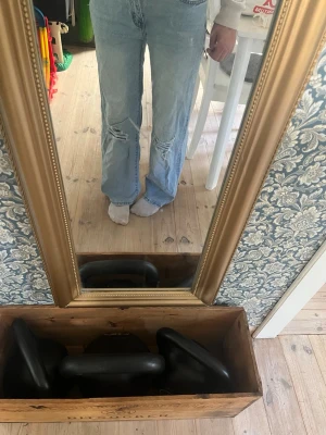 Ljusblå slitna raka jeans - Säljer ett par ljusblå jeans med raka ben och slitningar vid knäna. Jeansen har klassisk femficksmodell och hög midja. Perfekta för en avslappnad och trendig look.