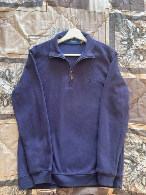 Blå quarter zip från Polo Ralph Lauren - Mörkblå långärmad tröja från Polo Ralph Lauren med quarter zip och liten broderad logga på bröstet. Tröjan har en klassisk krage och ribbade muddar vid ärmslut och nederkant. Perfekt för en avslappnad men ändå stilren look. Priset kan diskuteras 