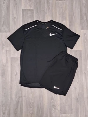 Nike set svart  - Snyggt svart träningsset från Nike med t-shirt och shorts. T-shirten har vita detaljer vid axlarna och Nike-logga på bröstet. Shortsen har elastisk midja och vit Nike-logga på benet. Perfekt för gymmet eller löpning.
