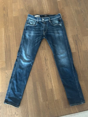 Replay jeans anbass hyperflex - Snygga blå Replay Anbass jeans slim fit med slitningar och tvättade detaljer. Klassisk femficksmodell med kontrastsömmar och läderpatch bak i midjan. Storlek: W32 L30
