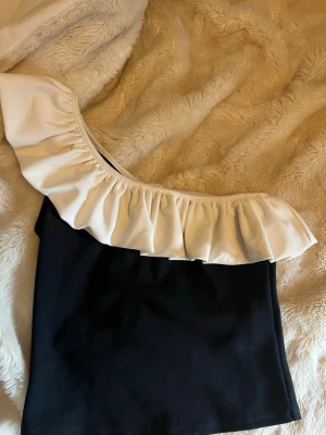 Svart oneshoulder topp med volang - Jättesnygg off shoulder topp från hm som är i jättebra skick, endast använd en gång 