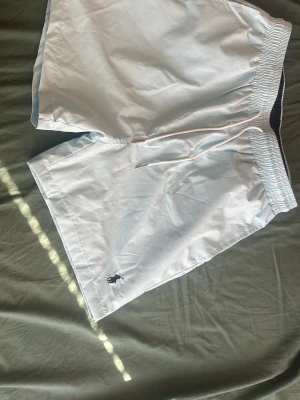Ralph lauren bad shorts - Snygga ljusblåa badbyxor med elastisk midja och dragsko. Klassisk passform och en liten broderad logga framtill. Bakficka med två metallöljetter för dränering. Perfekta för stranden eller poolen.