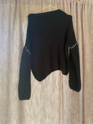 Svart stickad tröja med vita detaljer - Cool svart stickad tröja med vita sömdetaljer längs ärmarna. Tröjan har en avslappnad passform, ribbstickad struktur och långa ärmar. Perfekt för dig som gillar en unik och trendig look. Materialet känns mjukt och varmt.