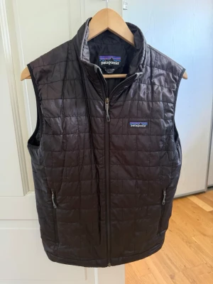 Svart dunväst från Patagonia - Snygg svart dunväst från Patagonia med quiltat mönster och hög krage.  Perfekt för lager-på-lager och håller dig varm under kyliga dagar. Mindre täcken på användning men inget märkvärdigt. Storlek S