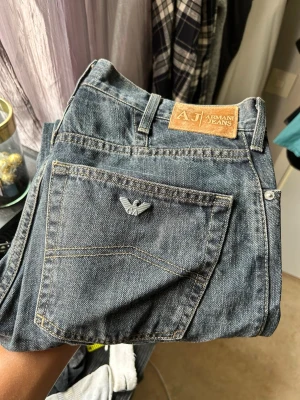 Mörkblå Armani Jeans raka - Säljer ett par mörkblå jeans från Armani Jeans med klassisk rak passform. Jeansen har en snygg bakficka med metallogo och läderpatch i midjan. Tillverkade i slitstark denim med tydliga sömmar och tidlös look.