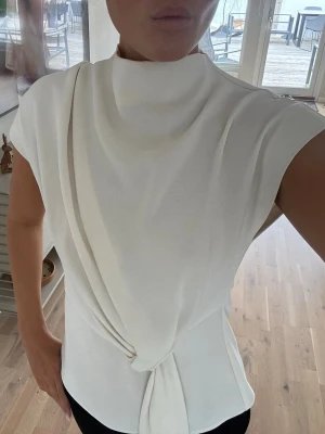 Vit omlottopp med knyt - Säljer en stilren vit topp från Zara med omlottdetalj och knyt framtill. Perfekt att styla med både jeans och kostymbyxor för en trendig outfit. Den är storlek xs men skulle säga de är xs-s 