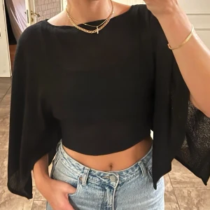 Stickad topp med capeärm / fladdermusarmar / breda armar H&M stl XS - Svart - Superfin och stilren stickad topp från H&M (Divided) i klassiskt svart. Toppen är i en croppad modell med långa, fladdrande capeärmar/ponchoärmar som ger en riktigt snygg och unik silhuett. Lätt att klä upp till fest eller använda till vardags med ett par höga jeans.  Storlek XS men passar även mig som bär S.   Mycket gott skick