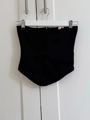 Svart korsett-topp - Snygg svart korsett-topp med markerade sömmar och en stilren, formad siluett. Toppen är axelbandslös och har en klassisk look som passar till många olika outfits. Perfekt för dig som vill ha en trendig och edgy stil💗