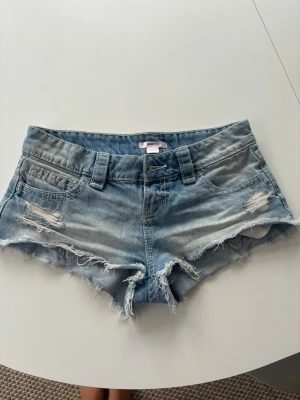 Ljusblå slitna jeansshorts - Säljer ett par ljusblå jeansshorts med slitna detaljer och fransig kant. De är i stl xxs men tycker att de mer känns som s-xs