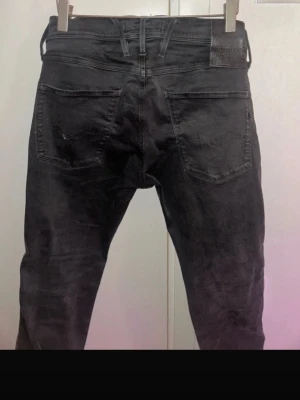 Svarta Replay - Säljer ett par svarta jeans från Replay med klassisk femficksdesign och raka ben. Jeansen har en diskret logga på myntfickan och är tillverkade i ett mjukt denimtyg som ger en skön passform. Perfekta för dig som gillar en stilren och enkel look. W28/L32