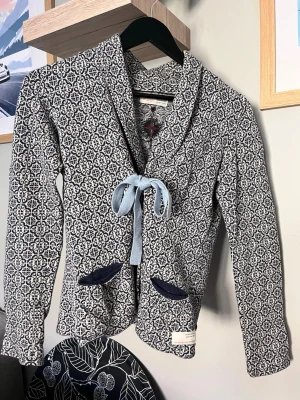 Mönstrad cardigan från Odd Molly - Supersnygg cardiganjacka från Odd Molly i blått och vitt mönster. Jackan har långa ärmar, två mörkblå fickor och knyts med ett ljusblått band framtill. Mjuk och skön kvalitet, perfekt för lager-på-lager-stil.
