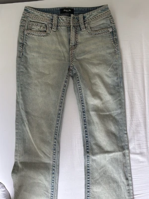 Ljusblå bootcut jeans Miss Me - Säljer ett par ljusblå bootcut jeans från Miss Me med dekorativa kontrastsömmar. Jeansen har klassisk femficksmodell, låg midja och slitna detaljer för en cool vintagekänsla. Perfekta för dig som gillar en avslappnad men trendig stil. JEANSEN ÄR ANVÄNDA FÅ GÅNGER MEN TYVÄR ÄR KNAPPEN AV! Det gåt dock enkelt att fixa! Därför säljs de billigt!