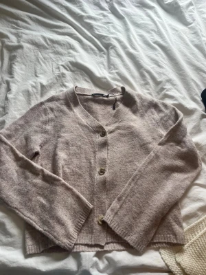 Beige kofta med knappar - Mysig beige kofta med v-ringning och tre stora knappar framtill. Koftan har långa ärmar och är stickad i ett mjukt material, perfekt för lager på lager. Enkel och stilren design som passar till det mesta.