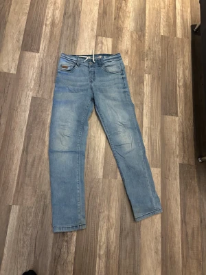 Ljusblå raka jeans med dragsko - Snygga ljusblå jeans med raka ben och dragsko i midjan. Jeansen har klassiska fem fickor och subtila slitningar vid knäna för en avslappnad look. Perfekta för en casual stil och tillverkade i mjukt denimtyg.