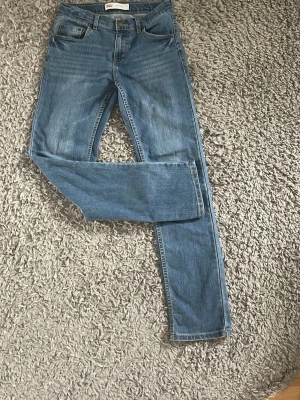 Blå raka jeans från Levi's - Klassiska blå jeans från Levi's med rak passform och fem fickor. Jeansen har normal midja och är gjorda i slitstarkt denimtyg. Perfekta till vardags och funkar till det mesta. Snygg tvätt och tidlös look.