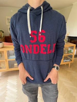 Bondelid hoodie herr broderad blå - Mörkblå hoodie från Bondelid.Rött tryck med "56 BONDELID".Klassisk passform med dragsko.Skönt material i fint skick.#bondelid#hoodie#herrtröja#blåhoodie#streetwear#casual#tröja#höstmode