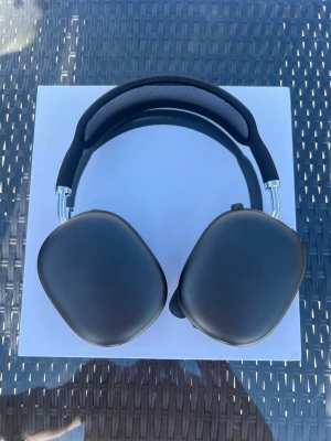 Svarta AirPods Max  - Stilrena svarta over-ear hörlurar med mjuka, ovala öronkuddar och justerbart huvudband. Hörlurarna har en modern design med metallbågar och mesh på insidan av huvudbandet för extra komfort. Perfekta för musik, gaming eller film.