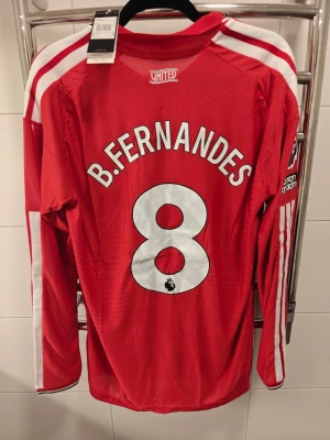 Nya Manchester United hemma tröja i spelar version, L - Säljer en röd långärmad Manchester United matchtröja från Adidas med B. Fernandes och nummer 8 på ryggen. Tröjan har vita detaljer, klubbmärke på bröstet, Premier League-märke på ärmen och sponsorlogga framtill. Perfekt för fotbollsfans!
