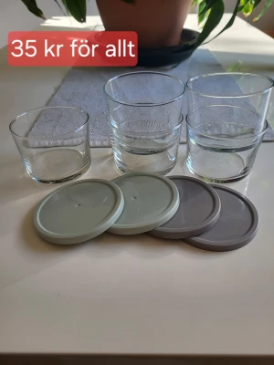 5 glas med 4 lock i olika färger - Säljer 5 genomskinliga glas i olika storlekar tillsammans med fyra plastlock i grå och ljusgrön färg. Glasen har enkel, rund form och locken passar perfekt till förvaring eller servering av dryck och snacks.