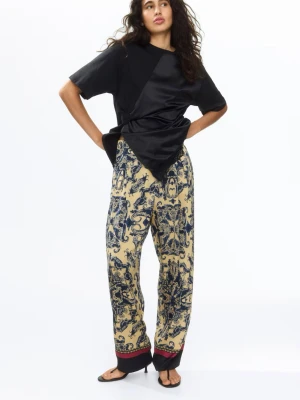 Mönstrade vida loungewear-byxor - Säljer ett par beige loungewear-byxor med blått barockinspirerat mönster. Byxorna har en avslappnad passform, resår i midjan med dragsko och kontrasterande mörkbruna muddar längst ner. Perfekta för chill dagar hemma. Helt nya, nypris: 299kr