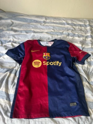 Barcelona 24/25  - Sesong 24/25. Storlek M, Säljer en officiell FC Barcelona matchtröja från Nike i rött och blått med klubbmärke. Tröjan har korta ärmar, rund hals och är tillverkad i lätt, ventilerande material. Perfekt för fotbollsträning eller att bära på läktaren eller i stan. 