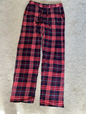 Rödrutiga pyjamasbyxor - Mysiga pyjamasbyxor i rött och svart rutigt mönster. Byxorna har resår i midjan och dragsko för bästa passform. Tillverkade i mjukt tyg, perfekta för chillkvällar hemma. Klassisk rak passform och långa ben.