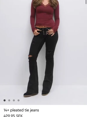 Svarta bootcut jeans  - Säljer ett par svarta bootcut jeans med snörning i midjan och slitna detaljer på benen. Jeansen har vida ben. Helt slutsålda och helt oanvända endast testade. Lapparna sitter även kvar lite små i storlek passar även som S