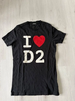 Svart Dsquared2 t-shirt med tryck - Svart t-shirt från Dsquared2 med stort tryck på framsidan där det står 'I ❤️ D2' i vitt och rött. Klassisk rund hals och korta ärmar. Perfekt för dig som vill ha en statement-tee med cool design.