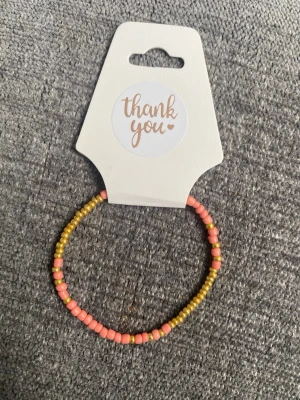 Armband med pärlor i gult och rosa - Snyggt armband med små pärlor i gult och rosa. Armbandet är elastiskt och passar de flesta handleder. Perfekt för att addera lite färg till din outfit och enkelt att matcha med andra smycken.