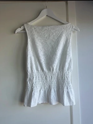 Vit spetsblus från Gina Tricot - Supersöt vit blus från Gina Tricot i storlek XS. Toppen har spetsdetaljer upptill och smockad midja som ger en snygg siluett. Perfekt till jeans eller kjol för en fräsch look. Ärmlös och lätt material, perfekt för varmare dagar. Aldrig använt!
