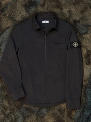 Svart overshirt från Stone Island - Snygg svart overshirt från Stone Island med dragkedja framtill, bröstficka med lock och den klassiska logotypen på vänster ärm. Overshirten har en rak passform och är tillverkad i ett mjukt, slitstarkt material. Perfekt för lager på lager och streetwear-stil.