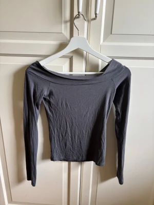 Mörkgrå långärmad topp BikBok - Snygg mörkgrå långärmad topp från BikBok med bred, offshoulder ringning. Tight passform som framhäver siluetten och passar perfekt till både jeans och kjol. Tillverkad i mjukt material som känns skönt mot huden.