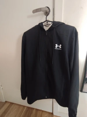 Under armour jacka  - Köpte den och den passade inte så helt oanvänd ny pris 750. Snygg svart jacka från Under Armour med dragkedja framtill och justerbar huva. Logga i vitt på bröstet ger en sportig vibe. Tillverkad i mjukt material som känns skönt mot huden. Perfekt för chill dagar eller när du vill ha en enkel och clean look.