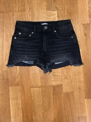 Svarta jeansshorts med fransig kant - Säljer ett par svarta jeansshorts från Roxy med fransig kant och klassisk femficksdesign. Shortsen har hög midja och råa avslut nertill för en avslappnad look. Perfekta för sommaren och passar till det mesta!