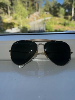 Ray-Ban aviator solglasögon guld - Klassiska Ray-Ban aviator solglasögon med guldfärgad metallbåge och mörkgröna glas. Snygg och tidlös modell som passar till det mesta. Perfekta för soliga dagar och ger en cool vibe till din stil.