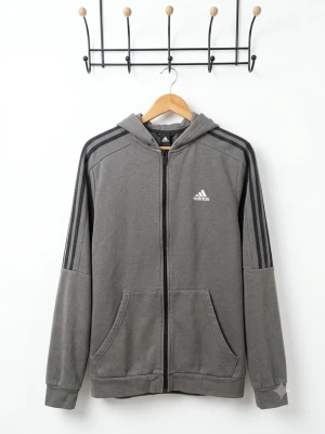 Grå zip hoodie från Adidas - Snygg grå hoodie från Adidas med dragkedja framtill och klassiska svarta ränder längs ärmarna. Adidas-logga på bröstet och två stora fickor fram. Tillverkad i mjukt material och har huva för extra chill vibe.