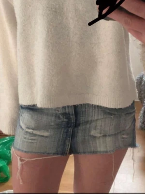 Jeanskjol med slitningar  - Säljer en blå jeanskjol med slitna detaljer och fransiga kanter. Kjolen har en klassisk femficksmodell och råa benslut för en avslappnad look. Perfekta till sommaren och lätta att matcha med olika toppar.