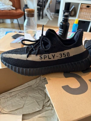 Adidas Yeezy Boost 350 V2 Core Black Green - Säljer ett par Adidas Yeezy Boost 350 V2 i svart med grön stripe och texten SPLY-350 på sidan. Skorna har en stickad ovandel, tjock räfflad sula och klassisk Yeezy-design. Perfekta för dig som gillar streetwear och vill sticka ut. Skorna är sällsynta då de inte haft någon restock på dessa. I nästintill nyskick, har använt ett fåtal gånger utan slitage som ni ser på bilderna.