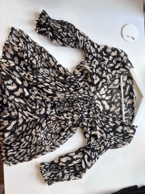 Svart och beige blus med leopardmönster - Snygg långärmad blus i transparent svart tyg med beige leopardmönster. Snörning i midjan för bättre passform