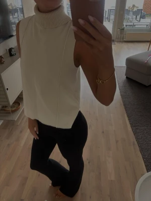 Vit ärmlös polotopp - Säljer en stilren vit polotopp utan ärmar. Toppen har hög, ribbad polokrage och rak passform. Perfekt att styla med både jeans och kjol för en clean look. Använd enbart en gång 