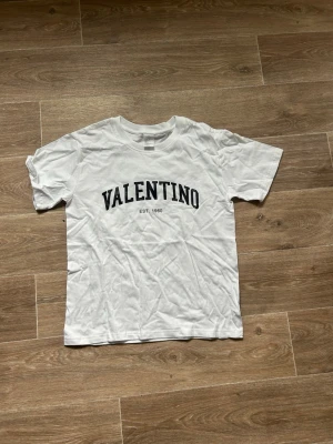 Vit Valentino t-shirt med tryck - Säljer en vit t-shirt från Valentino med svart texttryck på bröstet. Klassisk rund halsringning och korta ärmar. Perfekt till jeans eller shorts för en clean och stilren look.