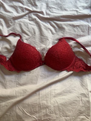 Röd spets-bh från Hunkemöller - Snygg röd bh från Hunkemöller med vadderade kupor och vacker spetsdetalj över hela bh:n. Axelbanden är justerbara och modellen har bygel för extra stöd. Perfekt för dig som vill ha något både bekvämt och stilrent. Den är tyvärr lite sönder vid bygeln vilket är bra att veta men det går säkert att försöka sy ihop!💓💓