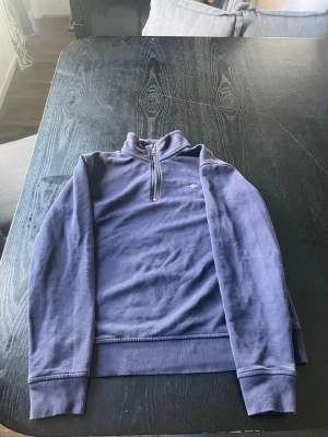 Blå halvzip tröja från Gant - Mörkblå långärmad tröja från Gant med halvzip och broderad logga på bröstet. Tröjan har ribbade muddar vid ärmslut och nederkant, samt en hög krage som ger en sportig och clean look. Perfekt för lager på lager och enkel att matcha. Jag köpte den för ny pris 1500kr