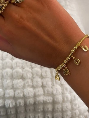 Guldarmband med bokstäver och pärlor - Stilrent armband i guldfärg rostfritt stål med ormkedja, dekorerat med runda pärlor och bokstäver som bildar ordet 'AMOUR'. Justerbar kedja med lås. Perfekt accessoar för att lyfta din outfit.