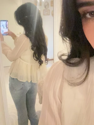 Vit volangblus med spetsdetaljer - Söt och luftig vit blus med volanger och spetsdetaljer vid halsen. Blusen har långärmade, transparenta ärmar och ett flowy fall som ger en romantisk vibe. Perfekt att styla med jeans för en trendig look.