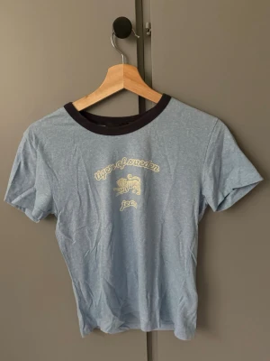 Blå Tiger of Sweden t-shirt - Snygg blå t-shirt från Tiger of Sweden Jeans med kontrastfärgad mörk krage och tryck framtill. Klassisk passform och korta ärmar, perfekt till jeans eller shorts. Skön och lätt i bomullsmaterial.
