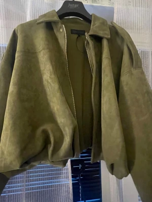 Olivgrön oversized skinnjacka - Snygg olivgrön skinnjacka i oversized modell med dragkedja framtill och klassisk krage. Jackan har breda ärmar och en avslappnad passform som ger en cool och trendig look. Perfekt för dig som vill sticka ut med en unik färg och stil.