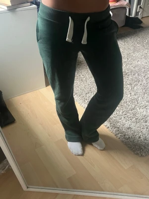 Mörkgröna mjukisbyxor med dragsko - Säljer ett par mörkgröna mjukisbyxor med vita dragsnören i midjan och fickor både fram och bak. Byxorna har rak passform och är gjorda i ett mjukt, bekvämt material som passar perfekt för chill dagar hemma eller när du vill vara extra comfy.