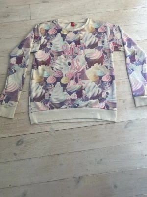 Cupcake-mönstrad sweatshirt - Säljer en långärmad sweatshirt från H&M med färgglatt cupcake-mönster och texten 'SWEET AS PIE' i rosa framtill. Tröjan har ribbade muddar vid ärmslut och nederkant samt rund halsringning.