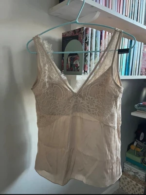 Beige spetsblus med djup v-ringning - Supersnygg beige blus/vit  med spetsdetaljer och djup v-ringning. Aldrig använd inga deftekter. Den är som ny